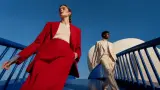 Two fashion models in red and cream suits walking through blue modern architecture