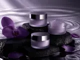 Lavender cosmetic jars arranged on black stones with orchids and rippling water